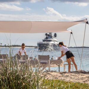 Yacht crew setting up a beach day with OKTO, a 218 foot ISA yacht for charter in the Mediterranean in the background.
