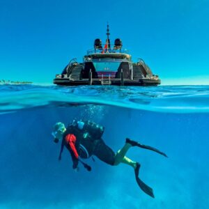 Diver swimming with OKTO, a 218 foot ISA yacht for charter in the Mediterranean in the background.